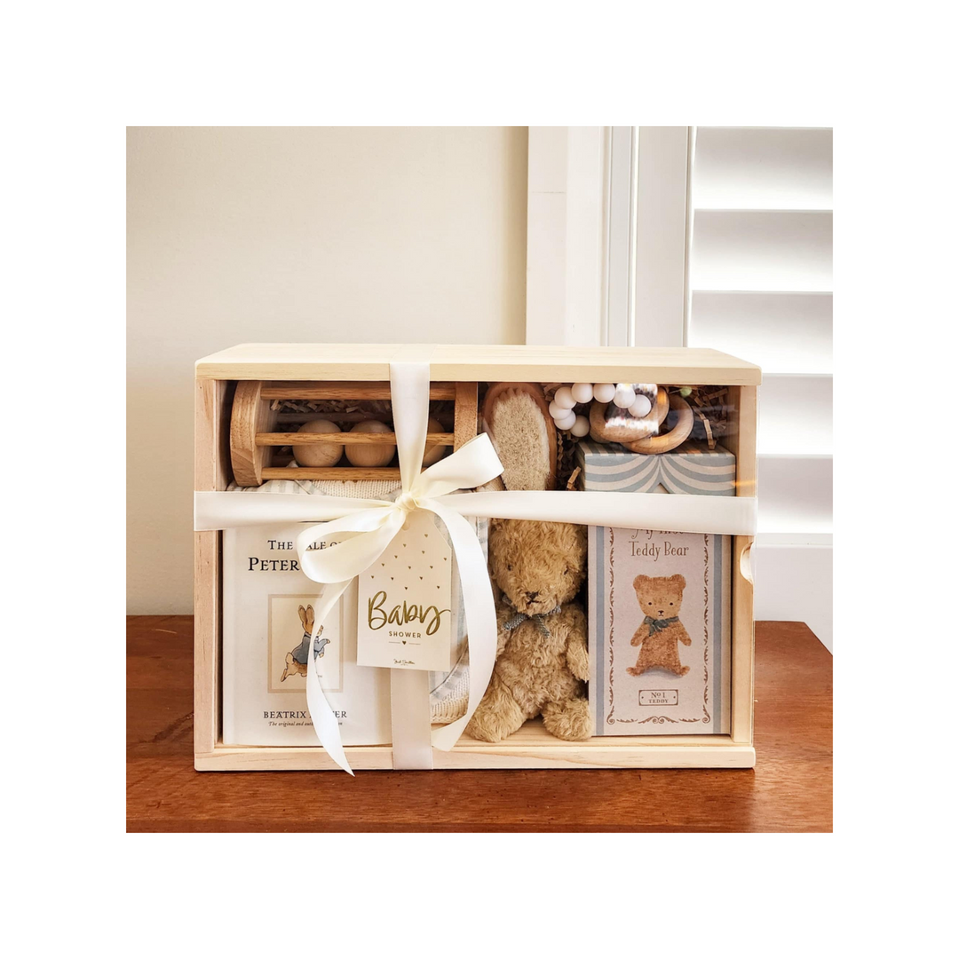 A beautifully arranged baby gift hamper featuring soft pastel-colored baby clothes, a plush toy, a baby blanket, and various baby care essentials, all meticulously packaged in an elegant wicker basket, adorned with a ribbon